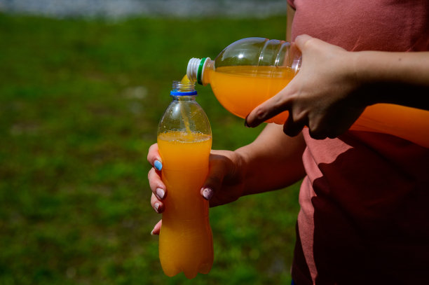 公园里，一名手持大塑料瓶的女子将橙汁装进小塑料瓶。户外图片下载