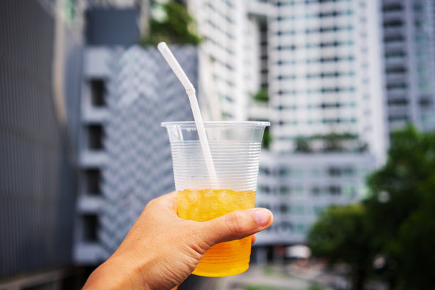 在建筑背景上，有人举起手，把冰镇的饮料举向天空图片下载