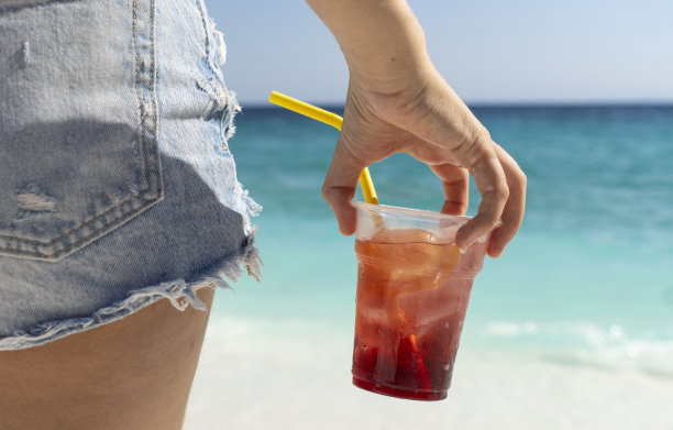 年轻的女孩拿着一杯新鲜的果汁加冰在海滩上图片下载