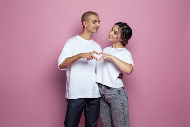 快乐的年轻男子和漂亮的年轻女子在粉红色的背景下一起做心图片下载