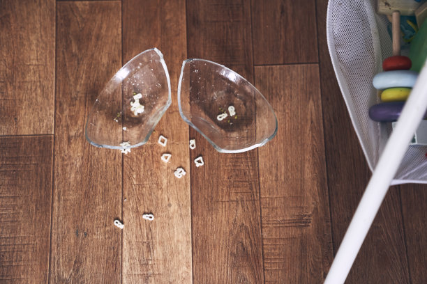 高脚椅上的一个小婴儿把一杯汤面掉在了木地板上。透明板分为两部分。面条以数字的形式出现。桌子是脏的。高画质照片图片下载