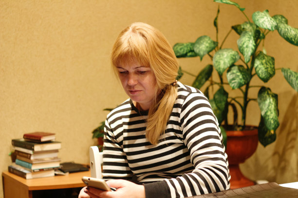 认真迷人的女人在家里工作时使用智能手机。年轻的法国金发女人扎着马尾辫。阅读新闻。优雅女人滚动手机。焦距模糊图片下载
