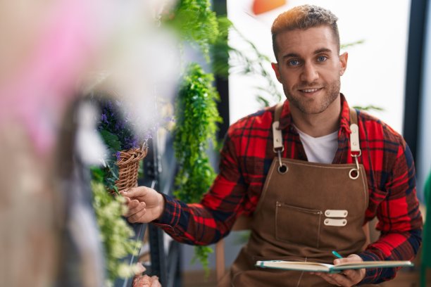 年轻的白人男子在花店拿着植物看笔记本图片下载