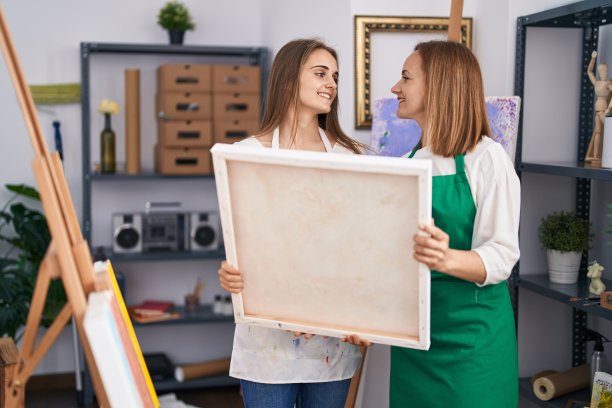 两位女艺术家在画室里自信地拿着画布微笑图片下载