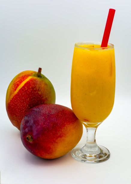 芒果汁。杯中有芒果汁和红色吸管，白色背景下有两个芒果。图片下载