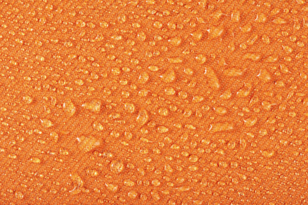 由防水纺织品制成的防水衣物或软垫家具。水滴在具有防水性能的橙色纺织品上。图片下载