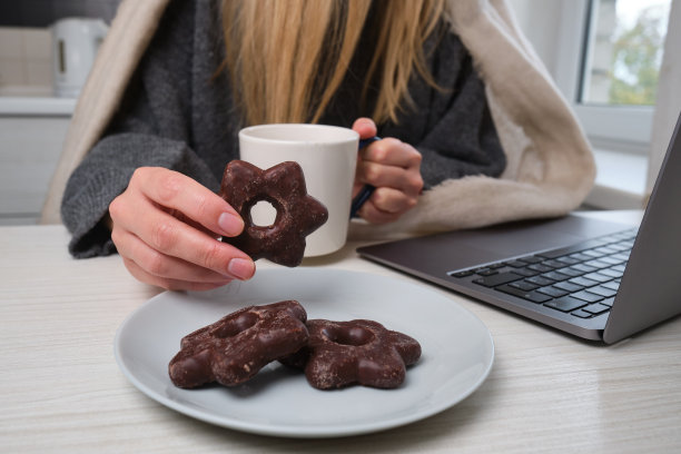 一个女人端着一杯茶坐在桌旁，手里拿着一块甜饼干。美味的传统甜点图片下载