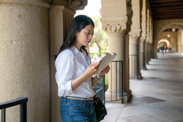 美国加州一所大学，一名亚裔华裔女大学生在一幢老教学楼的罗马式走廊外看笔记本图片下载