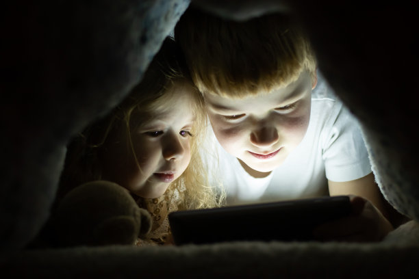 两个笑着的小弟弟和小妹妹在睡前用移动平板电脑看动画片图片下载