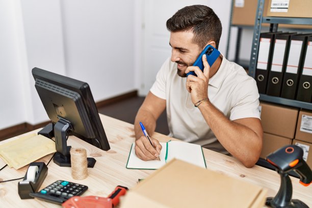 年轻的西班牙人在仓库用智能手机在笔记本上写东西图片下载