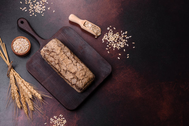 一块黑面包，上面有谷物，放在木砧板上图片下载