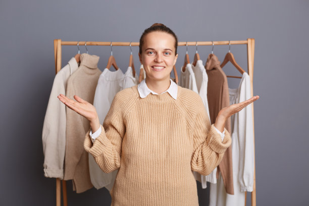 室内镜头的微笑满意的女造型师站在衣架架前与服装，摊开双手，呈现她的时尚酸痛与新系列。图片下载
