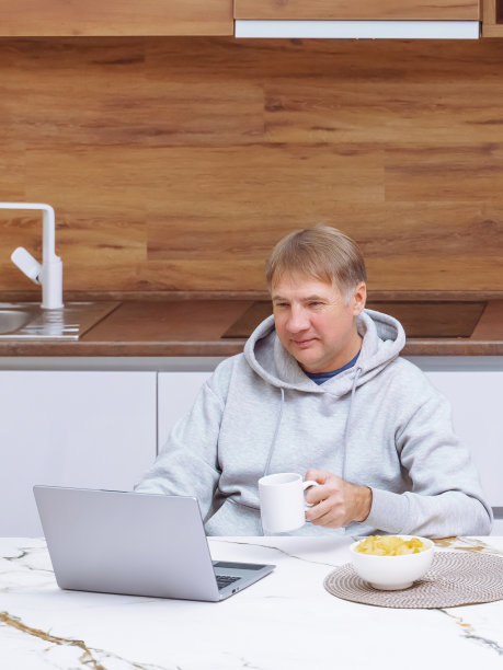 微笑的男人在现代厨房里用笔记本电脑工作，图片下载