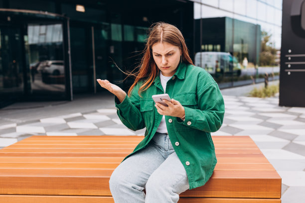 特写画像心烦难过，怀疑，不高兴，严肃的女人看着手机屏幕在户外。负面的人类情绪面部表情感觉。坏消息。女孩坐在城市街道的长凳上。图片下载