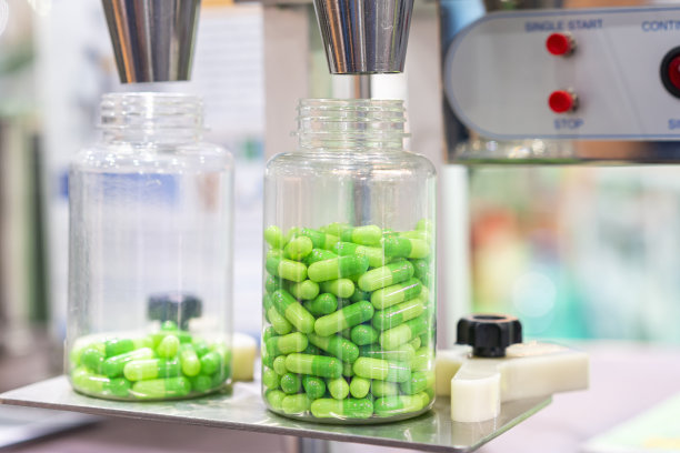 药用胶囊自动灌装计数机在生产过程中，将透明塑料瓶封闭在喷嘴分配器组件下图片下载