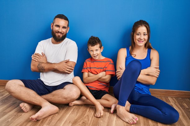 一家三口坐在家里的地板上，开心的脸抱着双臂微笑着看着镜头。积极的人。图片下载