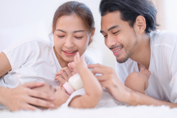 爸爸妈妈开心的逗着给刚在床上出生的亚洲婴儿喂奶图片下载