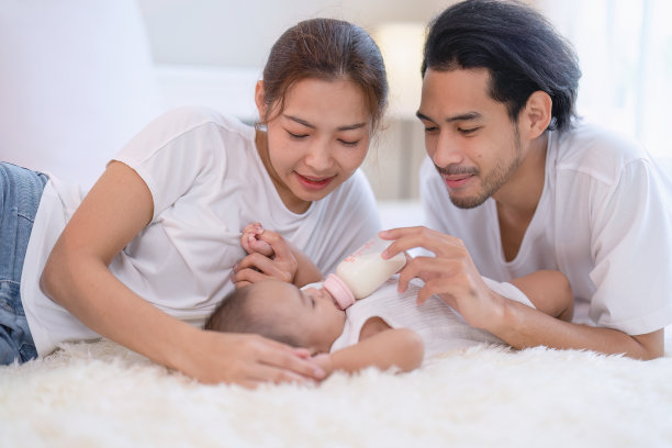 爸爸妈妈开心的逗着给刚在床上出生的亚洲婴儿喂奶图片下载