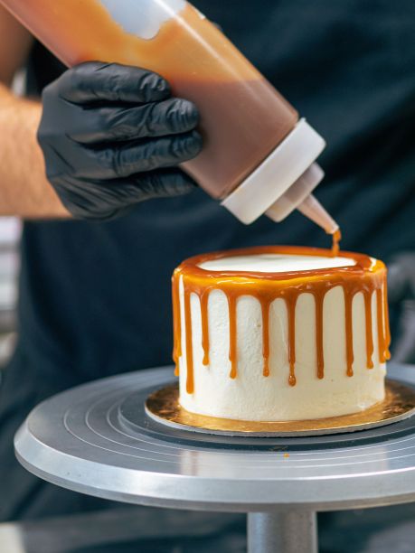 面包师傅用黑色手套用奶油和咸焦糖装饰纸杯蛋糕图片下载