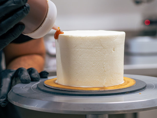 面包师傅用黑色手套用奶油和咸焦糖装饰纸杯蛋糕图片下载