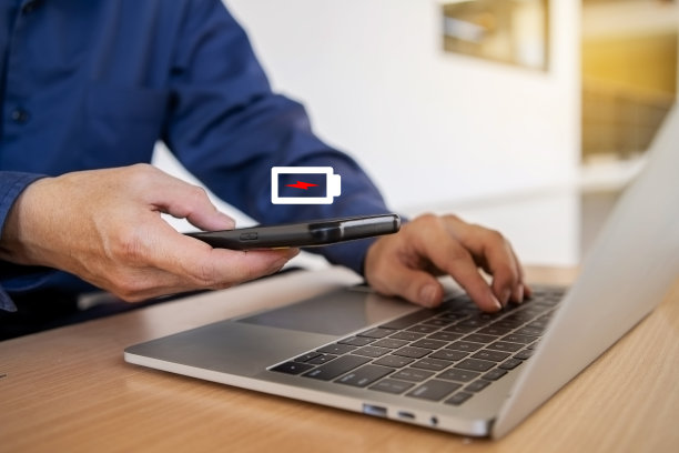 商人拿着一个低电量屏幕的手机在笔记本电脑上工作图片下载