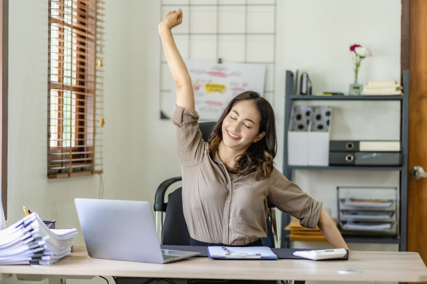 美丽年轻的亚洲女商人或女会计在工作中感到疲劳，在她的账目报告工作中伸展她的手。图片下载