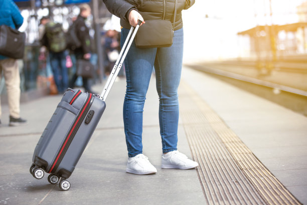 年轻女子提着手提行李在火车站等火车，交通概念图片下载