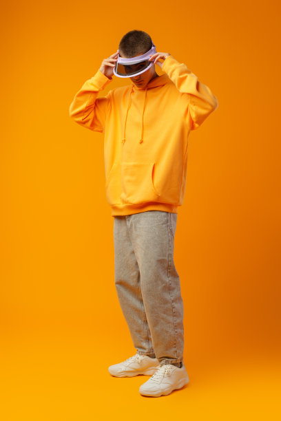 年轻的城市风格男子在运动衫和遮阳板上的黄色工作室背景图片下载