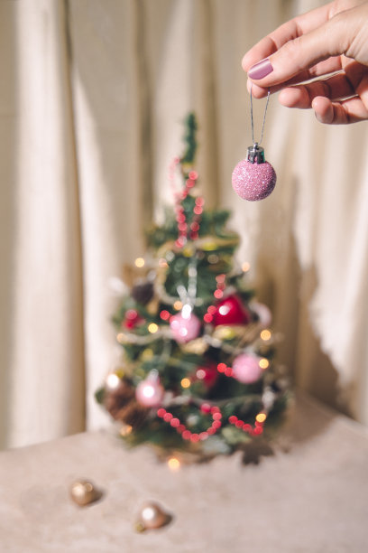 特写女性的手装饰圣诞树与一个闪亮的紫色小玩意。图片下载