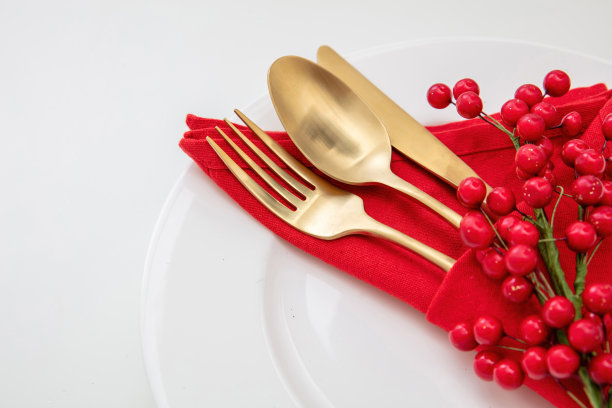 节日餐桌摆设。金色餐具和红布餐巾放在白色盘子上，特写图片下载