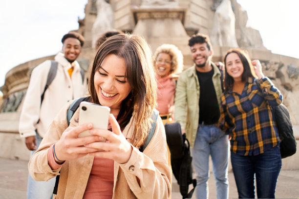 一个脸红而尴尬的女人看着手机，而一群朋友在后面等着。图片下载