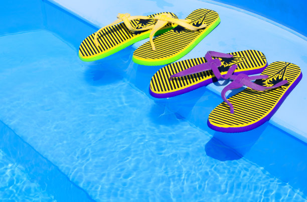 明亮和彩色的人字拖与海星在游泳池的背景。图片下载