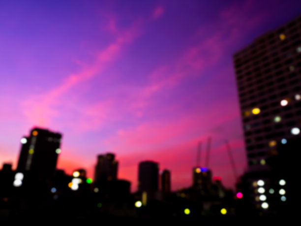 模糊轮廓的建筑，城市景观在紫色和蓝色的天空背景。夕阳西下，模糊的彩灯与商业建筑在黑暗中。抽象的夜晚城市背景。图片下载