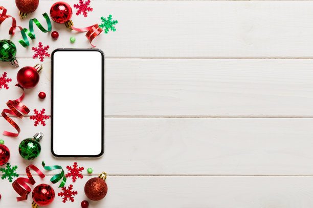 圣诞节网上购物从家里的电话与空白白色显示顶视图。智能手机与复制空间彩色背景与圣诞装饰球，。寒假销售背景图片下载