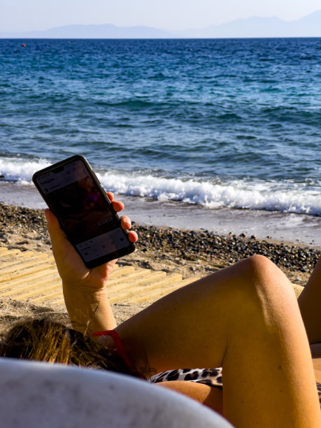 做日光浴的女人在看手机。图片下载