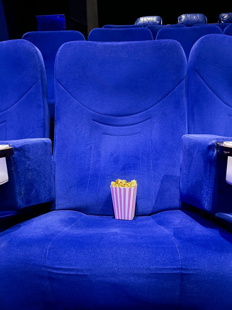 电影影院座位上的爆米花纸箱的形象，电影零食食品浴缸，蓝色天鹅绒座椅，重点在前景图片下载