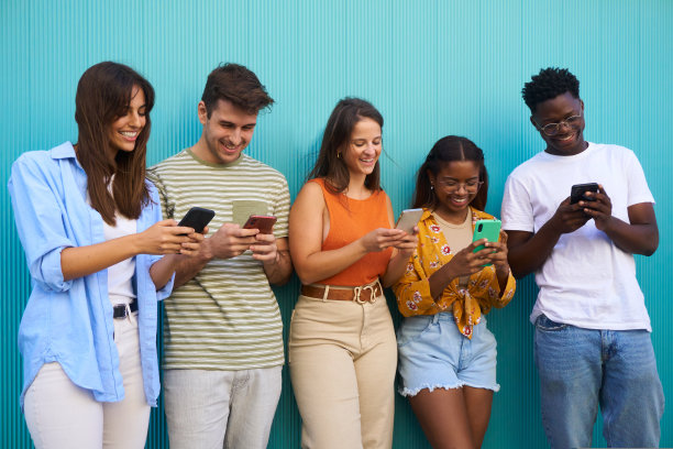 一群混合种族的年轻人在户外使用手机。被隔离在蓝色背景中的学生。图片下载