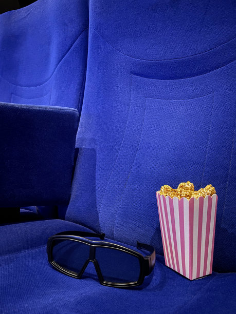 图像纸箱的爆米花在电影院电影院座位与3D眼镜，电影零食食品浴缸，蓝色天鹅绒座椅，重点在前景图片下载