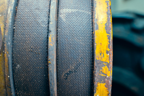 发动机特写上的两条粗皮带。传动带陈旧破旧，上有黄色滑轮，背景模糊。农业工业产品图片下载