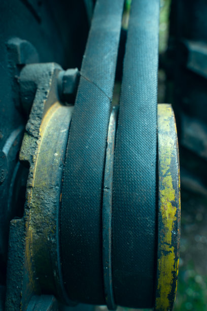 发动机特写上的两条粗皮带。传动带陈旧破旧，上有黄色滑轮，背景模糊。农业工业项目，垂直照片图片下载