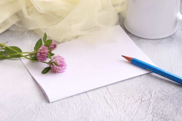 用铅笔清空便条纸。一枝三叶草放在桌上和马克杯上，网眼织物质地布。温馨的家庭时光。图片下载