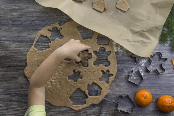 新年和圣诞节装饰在一个木制表面与橘子和一棵圣诞树。一个小孩的手在制作制作人形姜饼的模具。图片下载