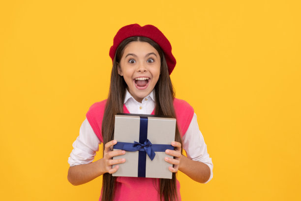 惊讶的十几岁女孩在法国贝雷帽手持礼物或礼盒上的黄色背景，惊讶图片下载