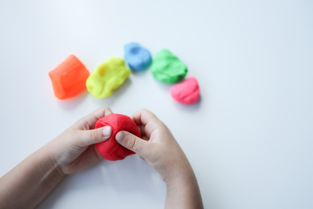 婴儿的手在白色的桌子背景上捏捏红色的黏土。特写镜头。幼儿的发展。准备制作不同颜色形状的材料图片下载