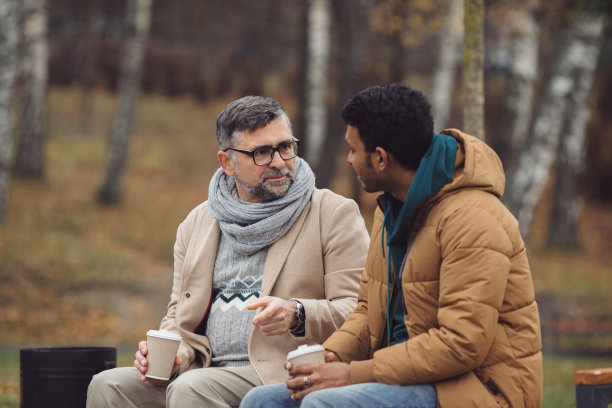 朋友，一个学长和一个年轻人坐在公园的长椅上，在秋天的公园里聊天。图片下载