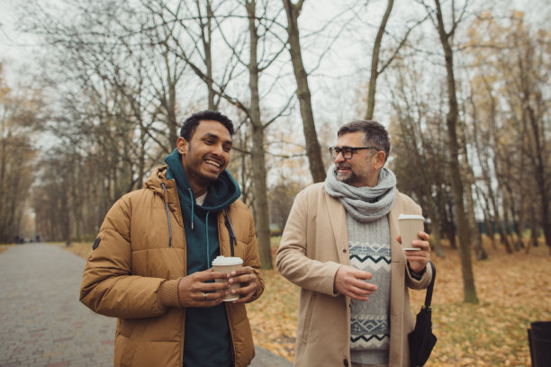 朋友，一个老人和一个年轻人一起在秋天的公园散步，聊天，喝咖啡。图片下载