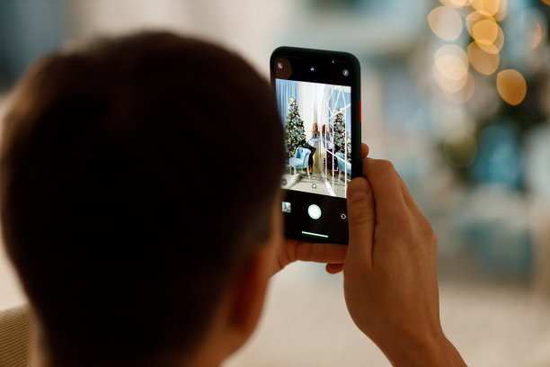 一名男子在圣诞树旁用手机给女友拍照图片下载