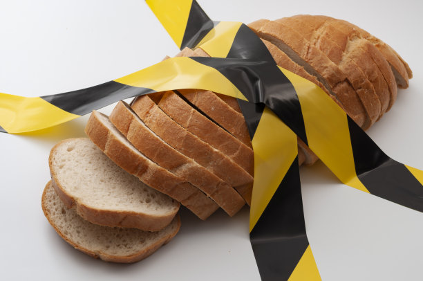 切片面包和白色背景隔离的黄色警告胶带代表粮食不安全、饥饿警告和危险加工谷物图片下载