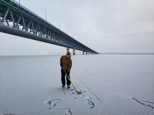 在乌里扬诺夫斯克，一名曲棍球运动员站在伏尔加河上，背景是一座大桥。图片下载