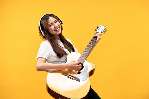 年轻的亚洲妇女戴着耳机和白色短袖衬衫，弹吉他和唱摇滚图片下载